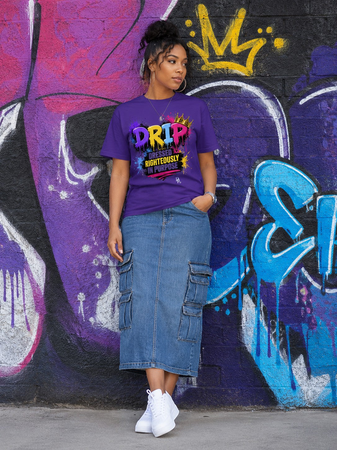 Woman wearing a purple Dunamis Perception DRIP graphic tee with a denim cargo skirt against a graffiti wall.